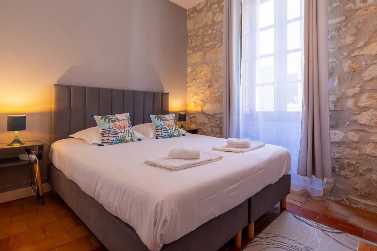 Chambre double avec lit queen size, mur en pierre et grande fenêtre
